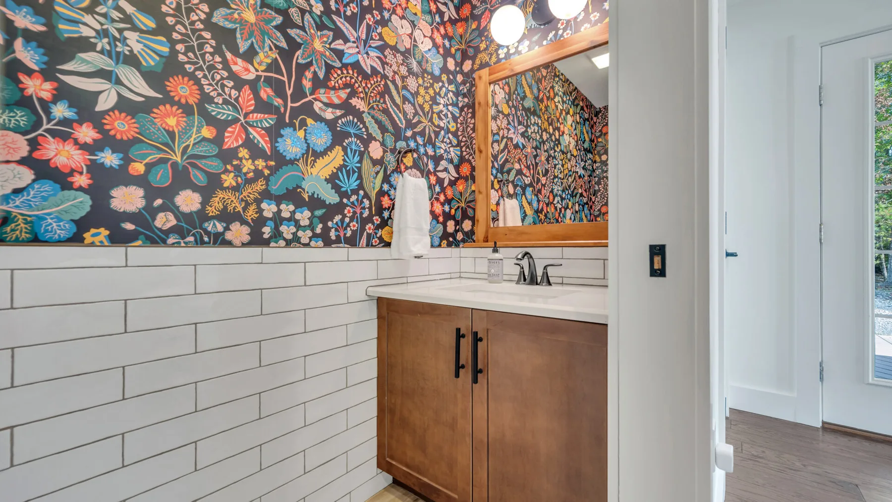 A bathroom vanity with a sink sits beneath a colorful floral wall covering.