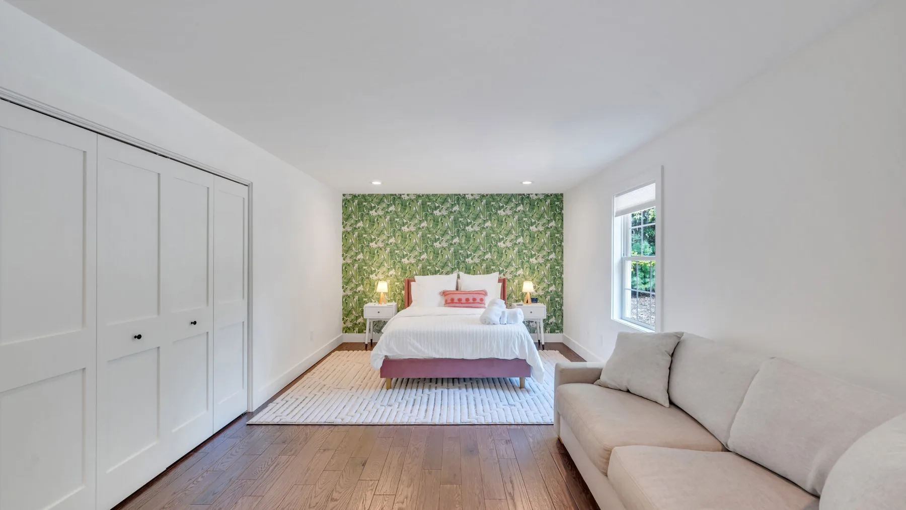 A bright bedroom with a bed against a leafy wall and seating nearby.