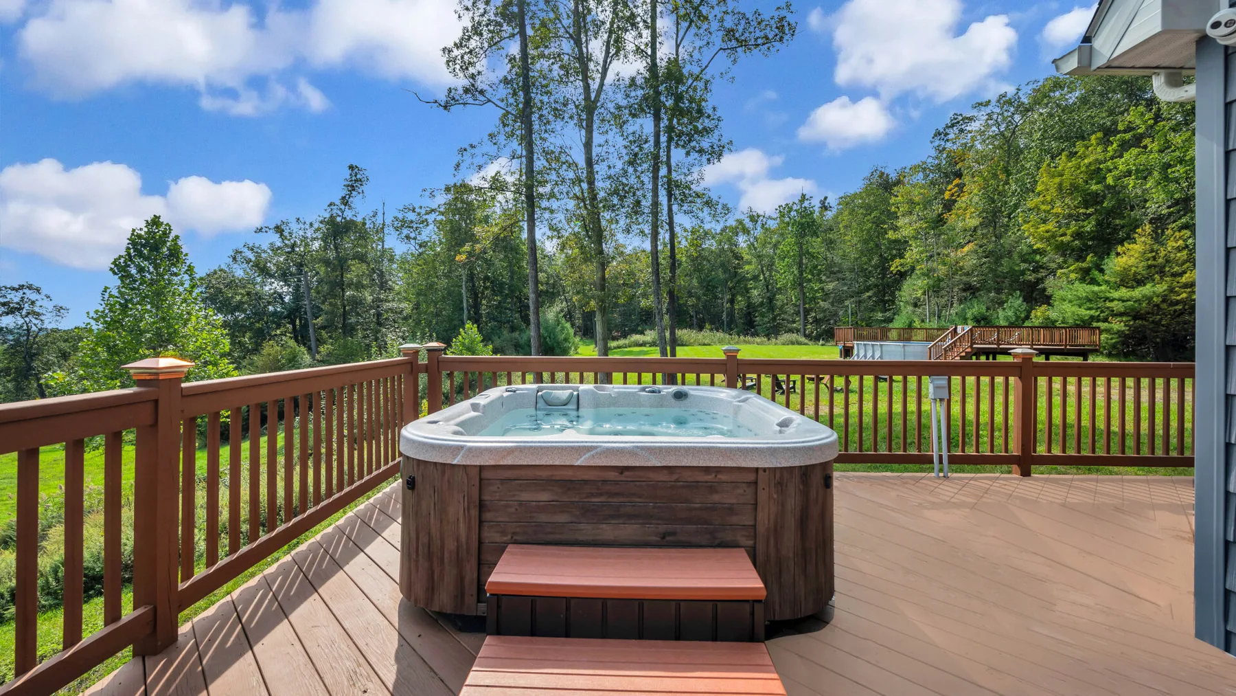 An outdoor deck features a hot tub overlooking a grassy yard and trees.