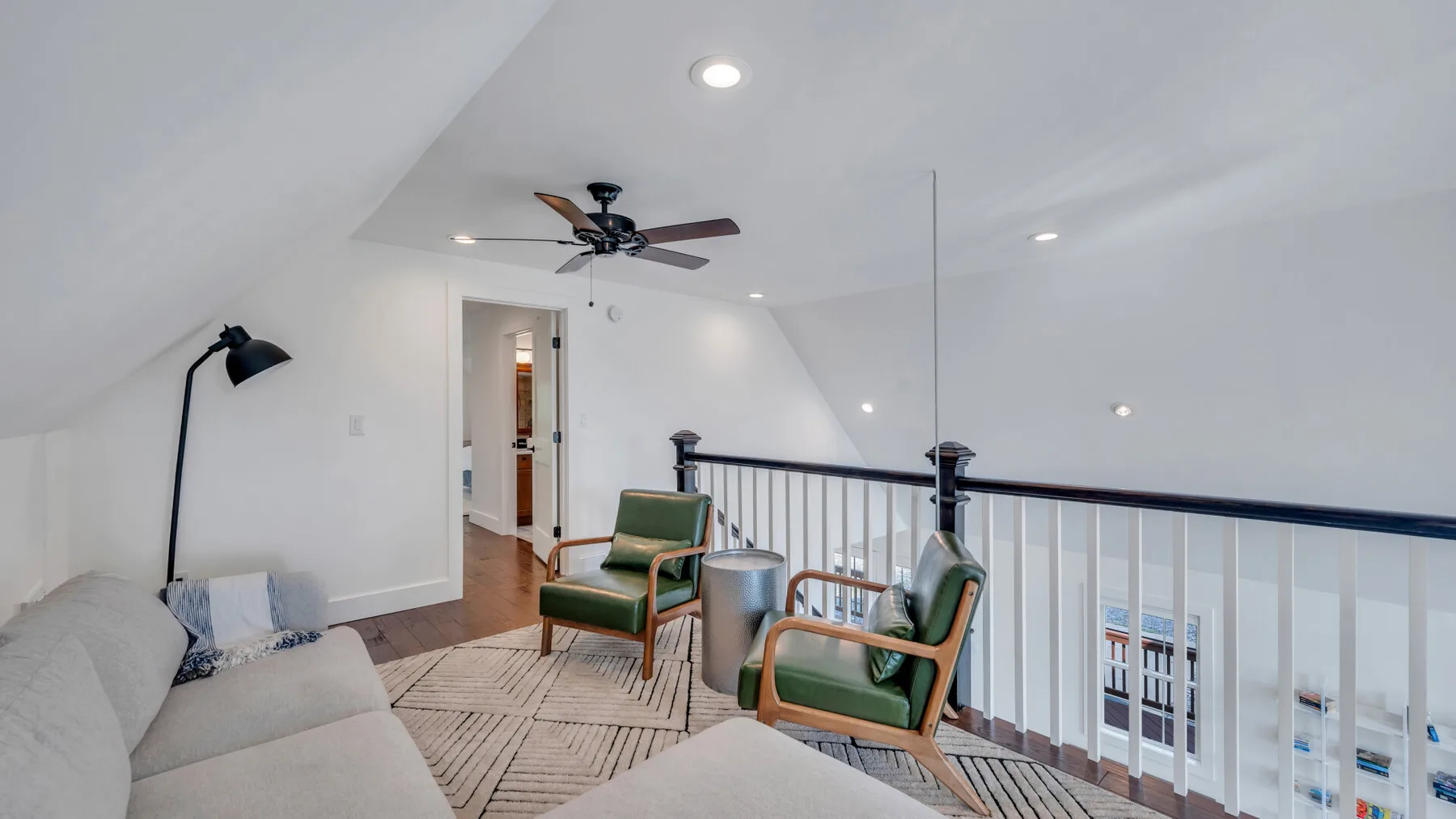A bright loft sitting area has seating, a rug, and a railing overlooking the space below.