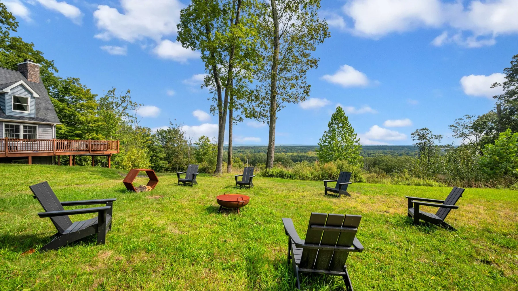 A grassy outdoor seating area has scattered chairs and a wide countryside view.