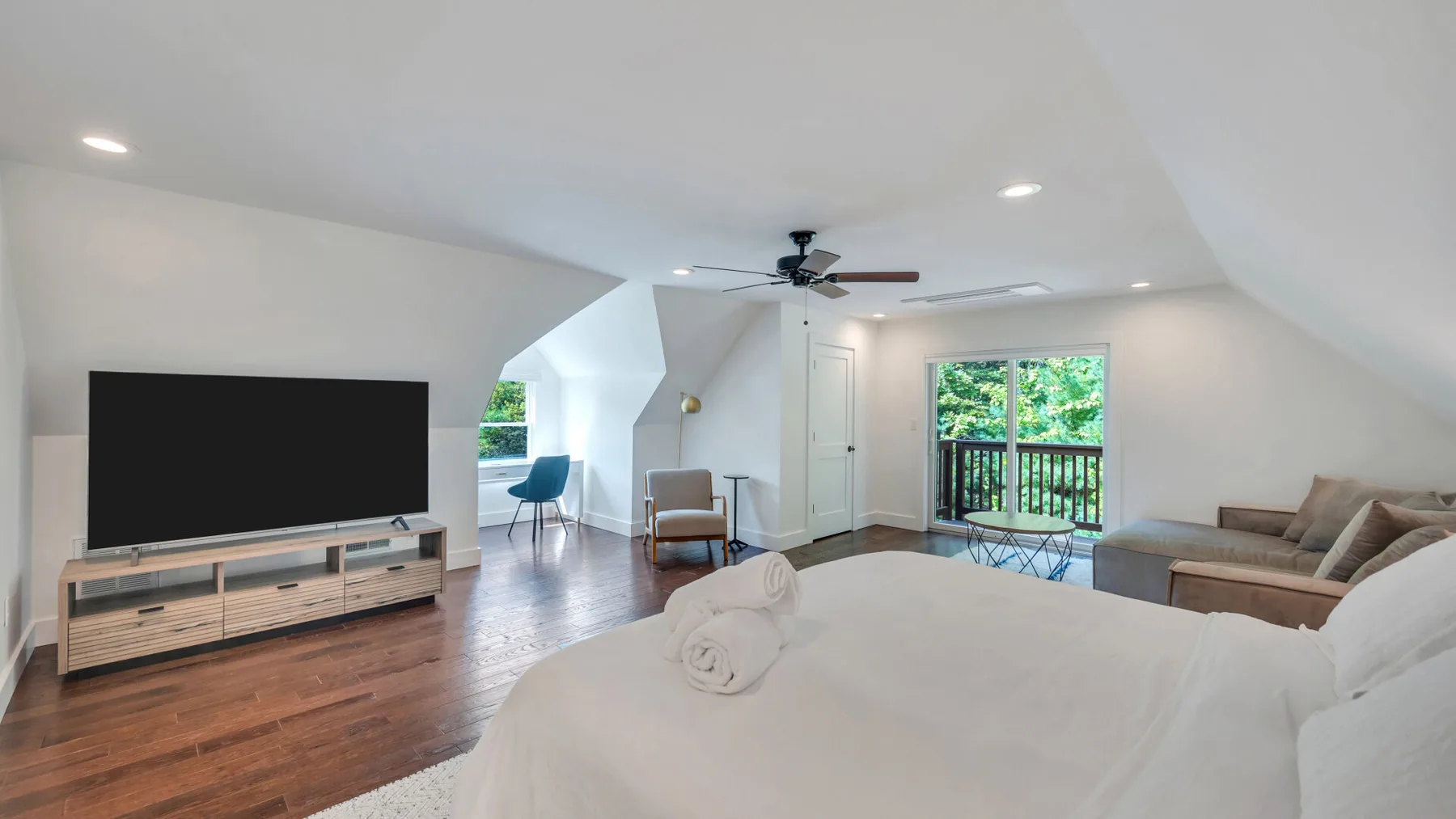 A bright bedroom with a large bed, television, and balcony doors.