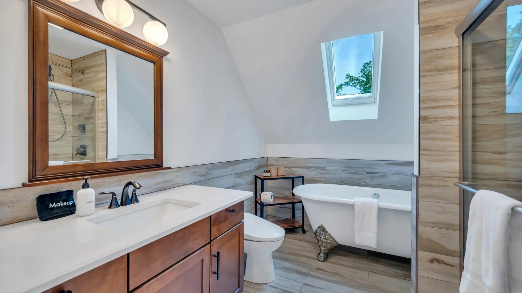 A bright bathroom has a vanity, toilet, and bathtub beneath a small window.