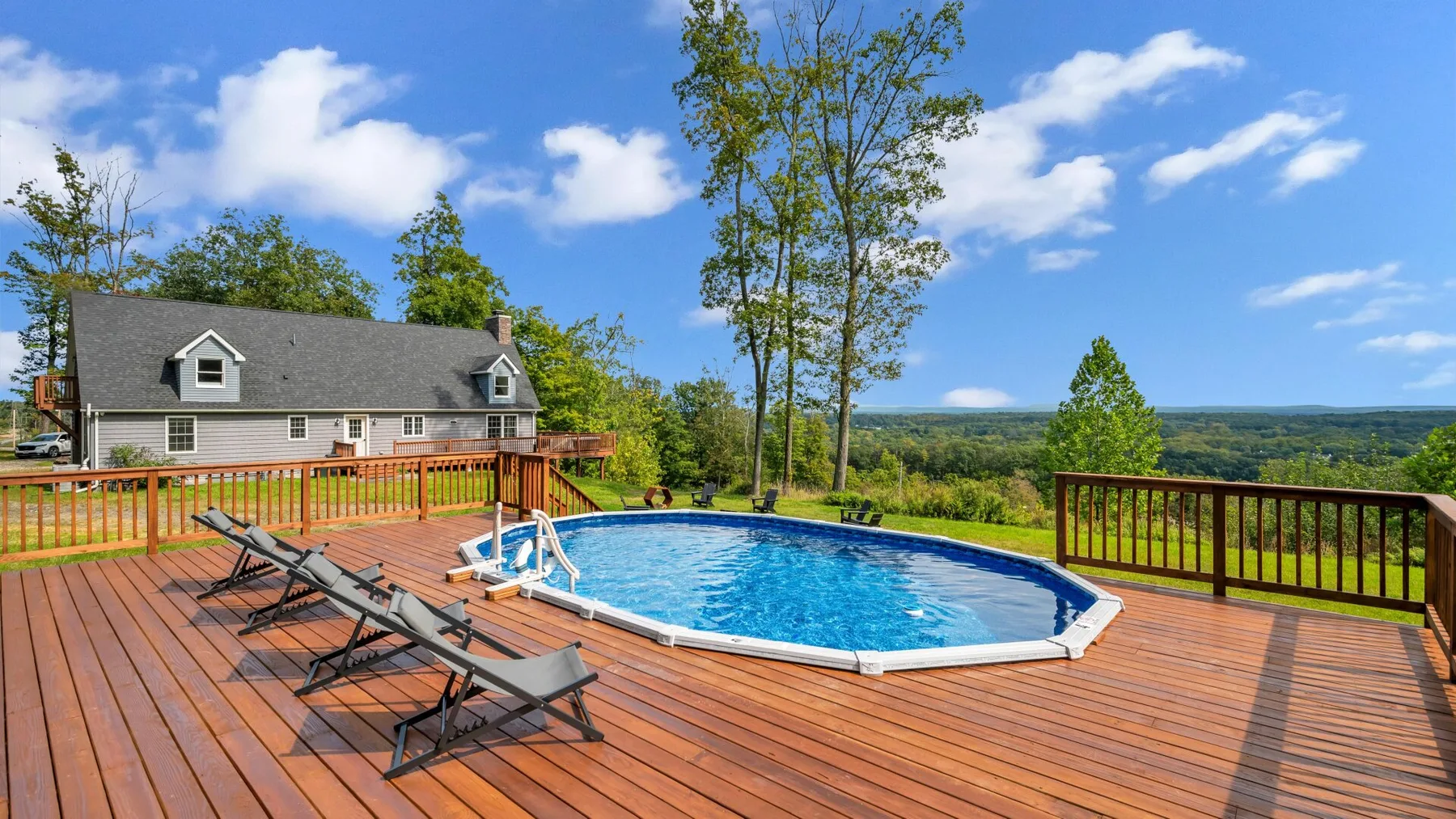 An outdoor pool sits on a spacious wooden deck beside a house.