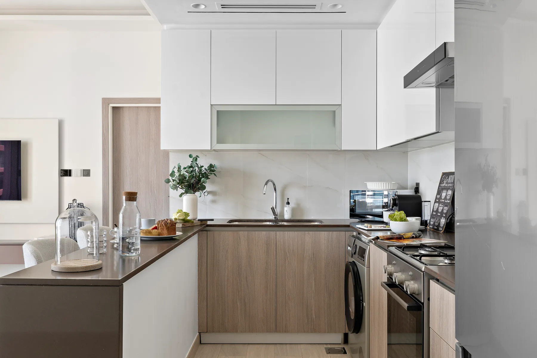 Una cocina moderna con gabinetes claros, muebles inferiores en tono madera y un fregadero central.