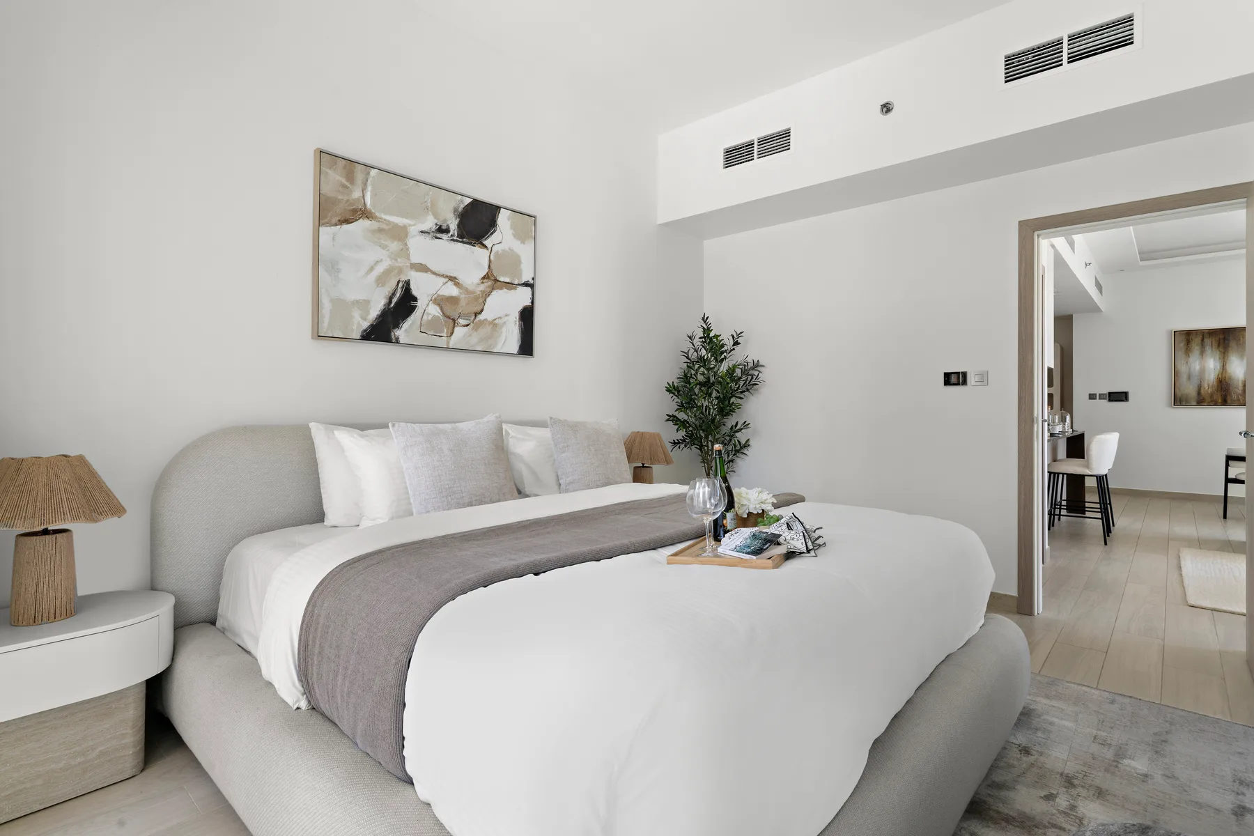 Un dormitorio luminoso con una cama bien tendida y arte abstracto encima.