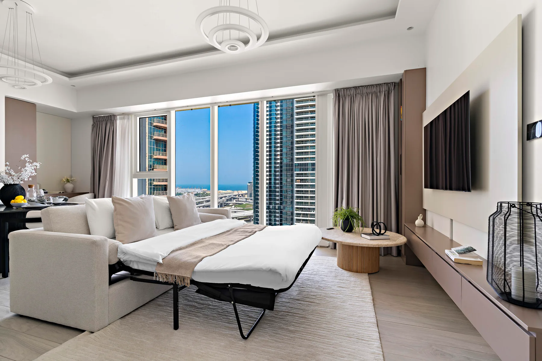 Un dormitorio luminoso con una cama grande, asientos y ventanales con vistas a la ciudad.