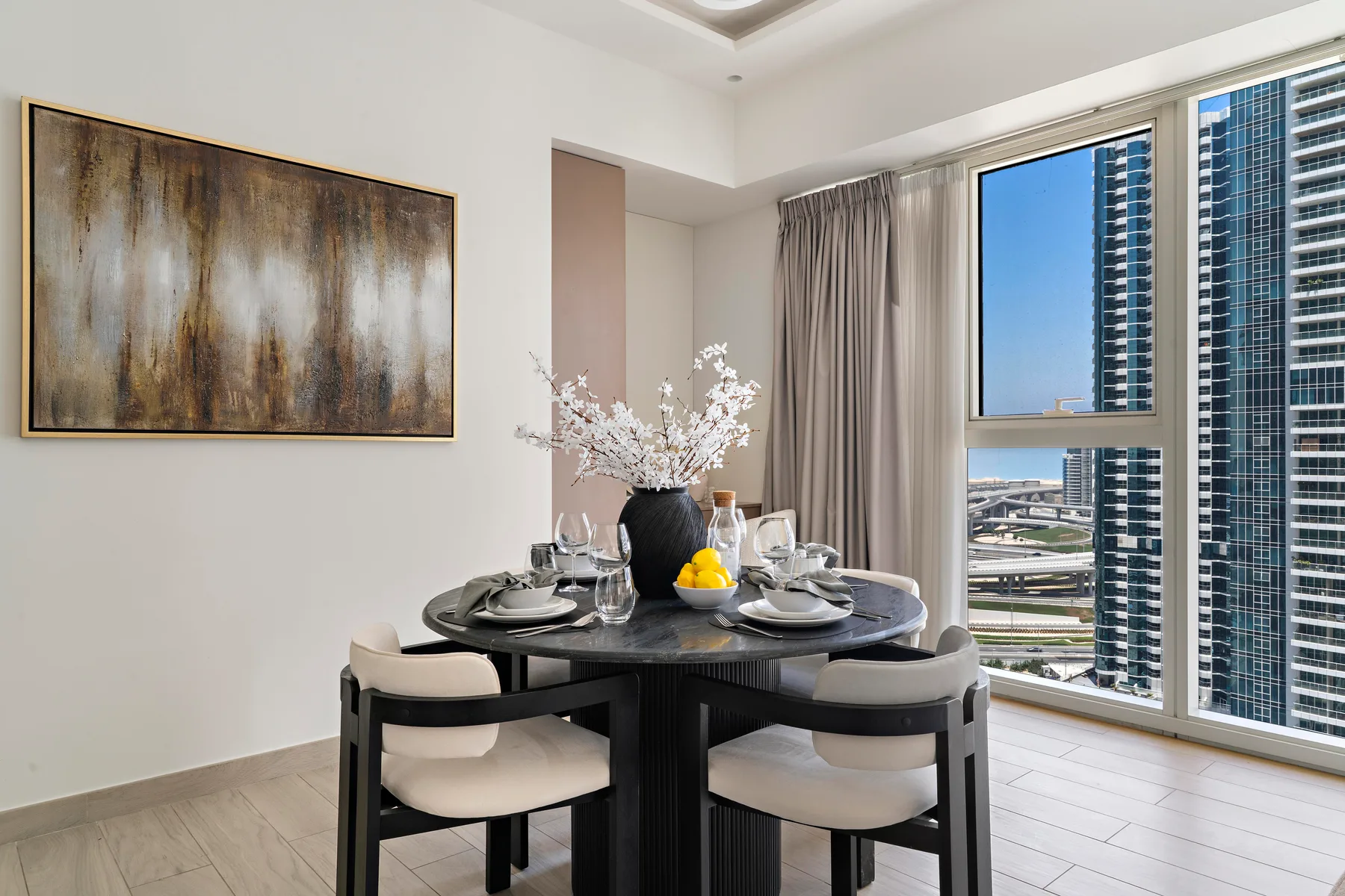 Un comedor con la mesa puesta junto a grandes ventanas con vistas a edificios cercanos.