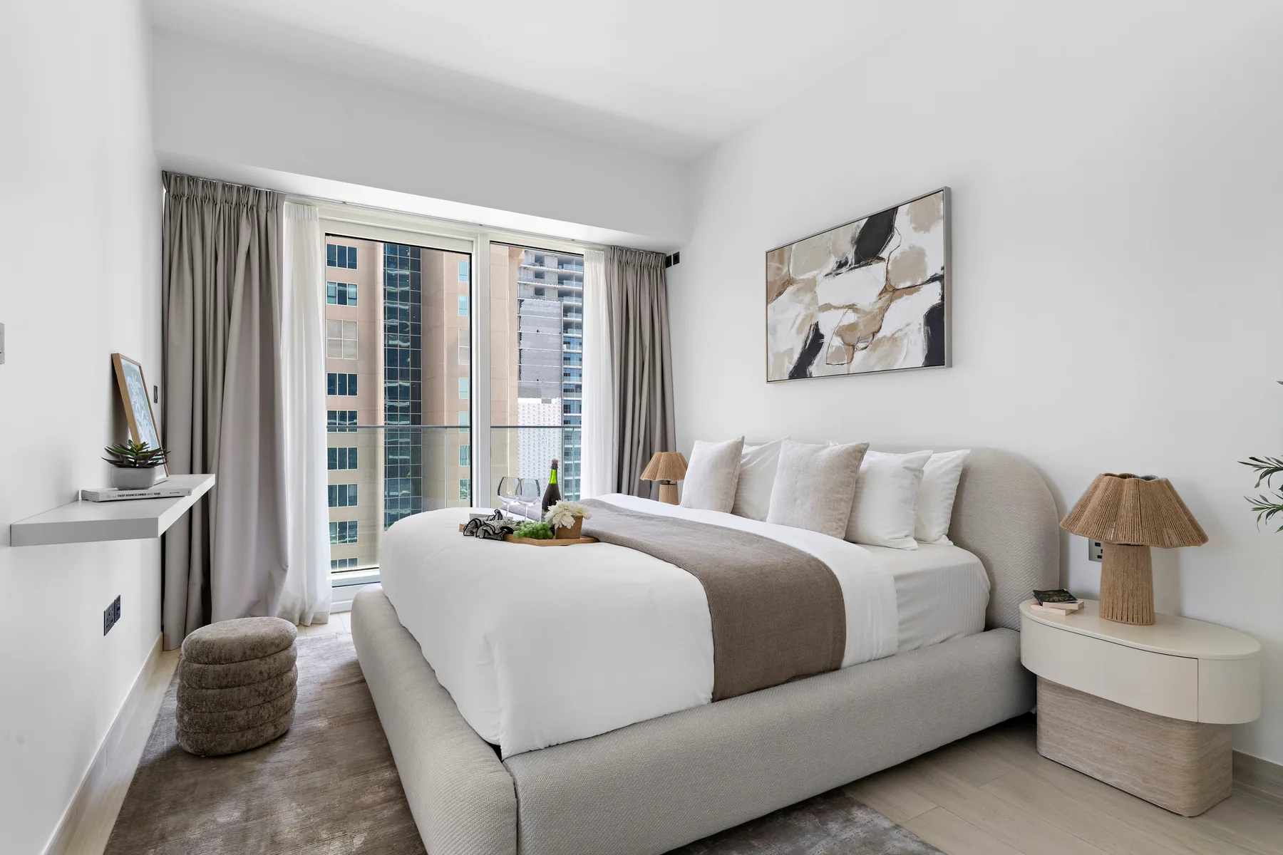 Un dormitorio luminoso con una cama tendida junto a ventanas altas y cortinas.