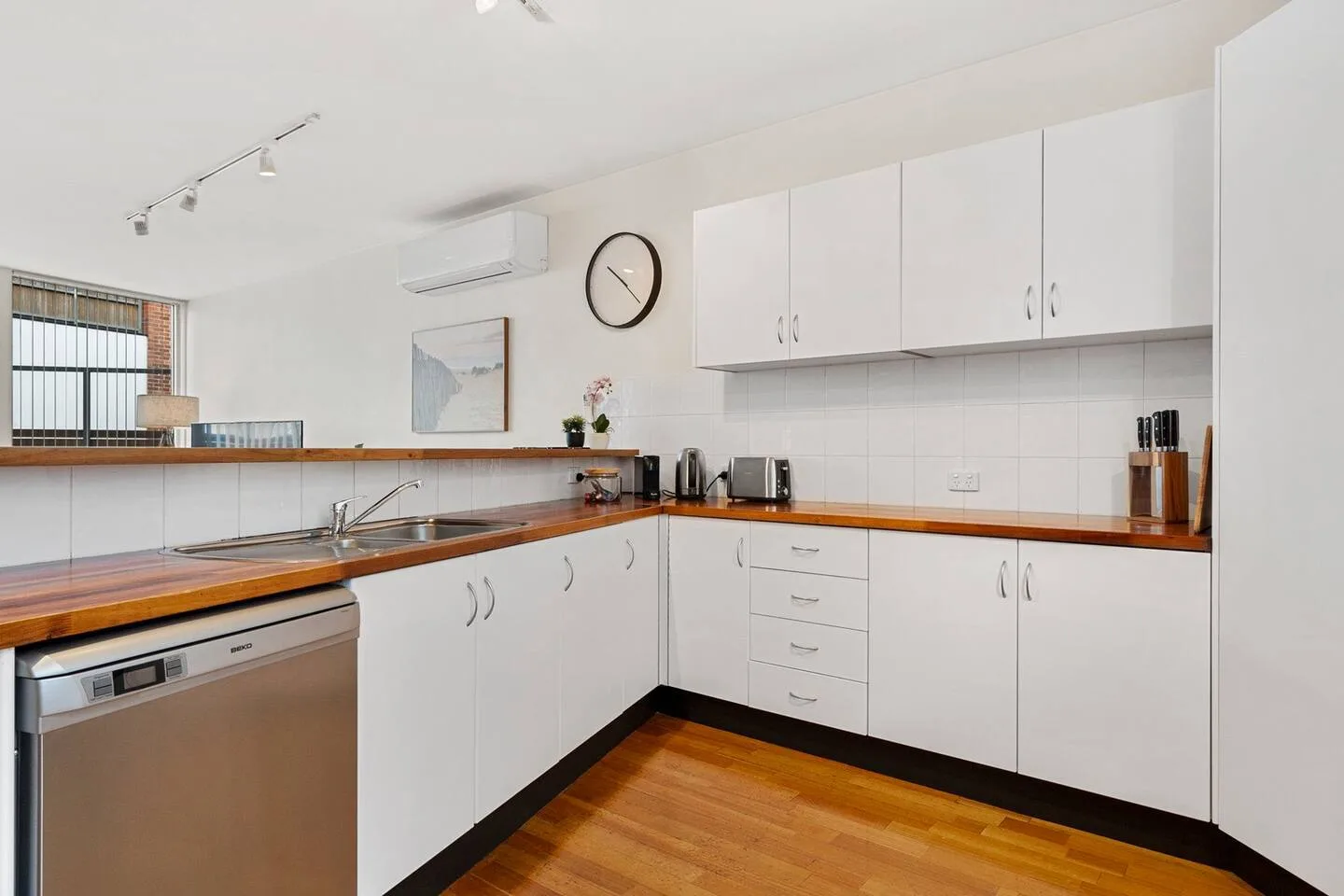 Una cocina luminosa con armarios blancos, encimeras de madera y un fregadero.