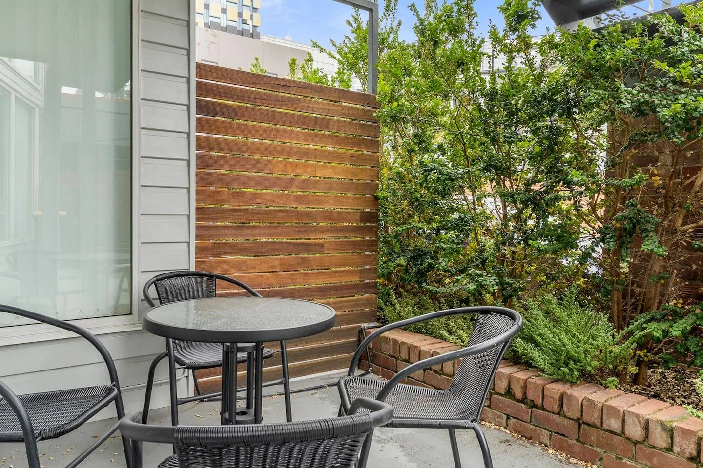 An outdoor patio has a round table and seating beside a wooden privacy screen.
