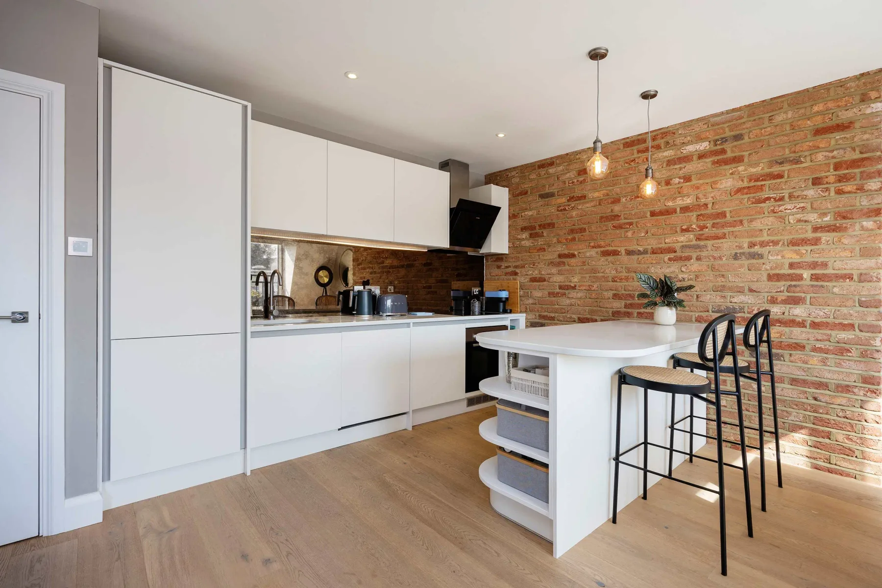 Una cocina moderna con gabinetes blancos, una isla central y una pared de ladrillo visto.