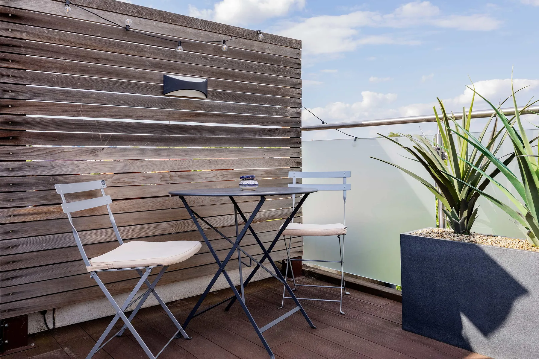 Un espacio de estar en un balcón con una mesa pequeña, una pantalla de madera y plantas en macetas.