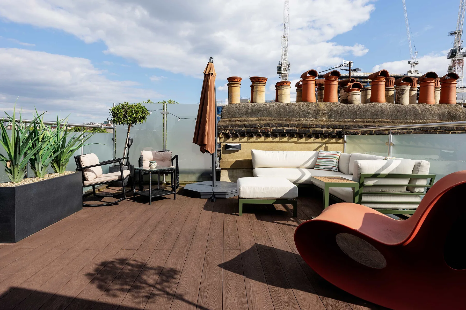 Una terraza en la azotea con asientos al aire libre, jardineras y vistas a los tejados cercanos.