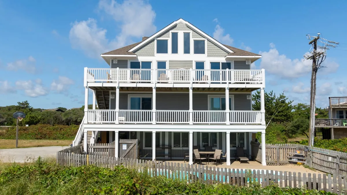 Una gran casa blanca de estilo costero con balcones está detrás de una cerca baja.