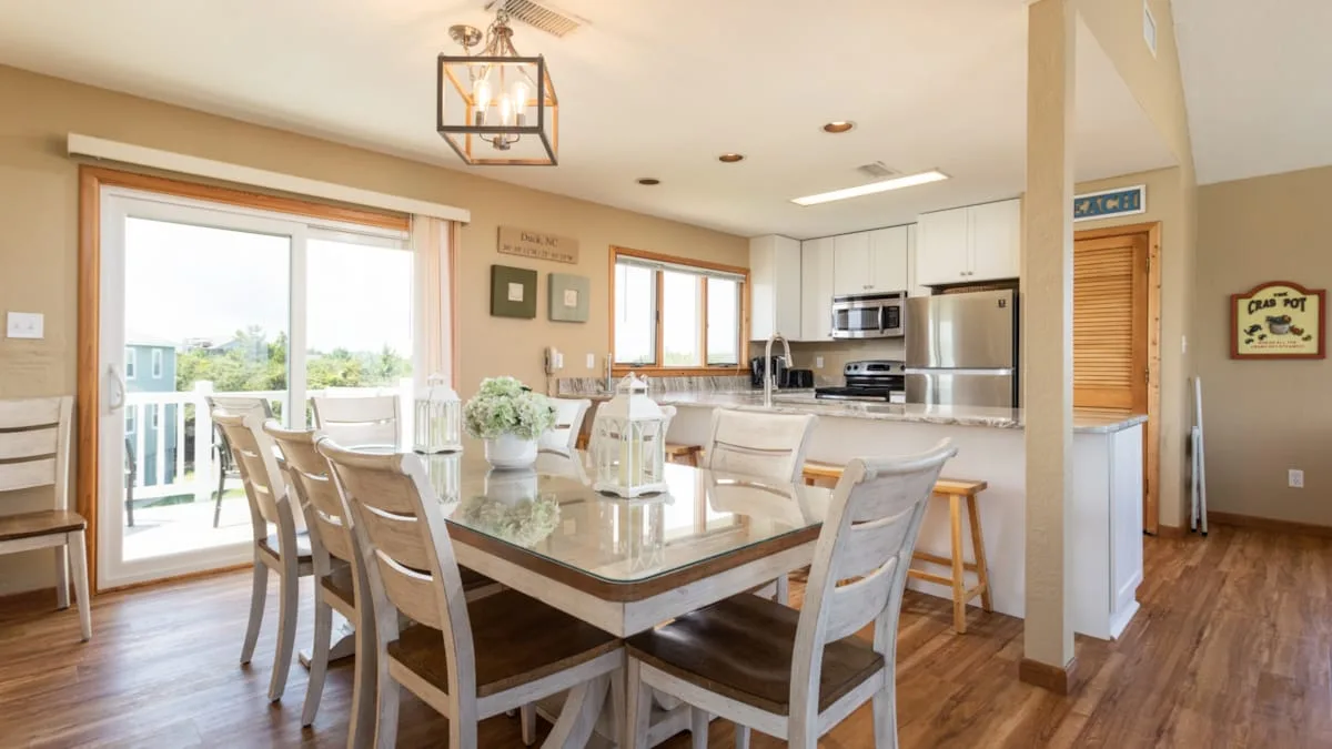 Un espacio abierto de comedor y cocina con una mesa grande y ventanas luminosas.