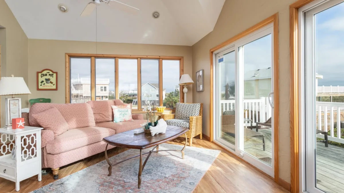 Una sala luminosa con asientos rosados y grandes ventanas con vista a una terraza.