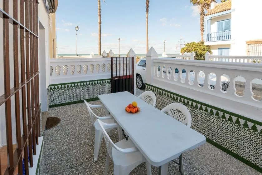 A tiled outdoor dining area with a white table and chairs beside a decorative railing.