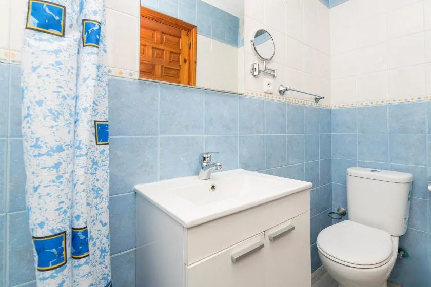 A tiled bathroom with a sink and toilet beside a patterned shower curtain.
