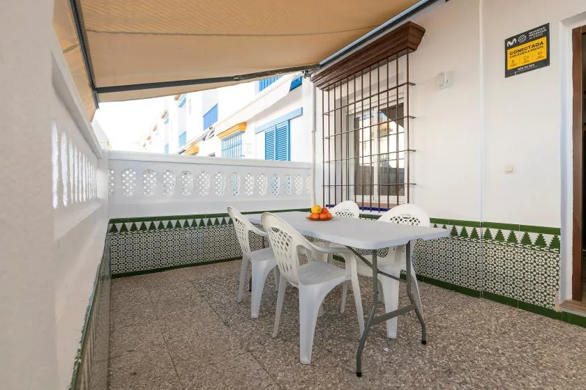 A covered outdoor dining area has a table and white plastic seating.