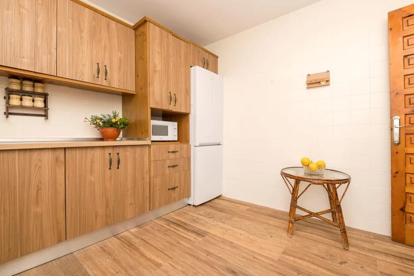 A kitchen with wooden cabinets, a refrigerator, and a small table.