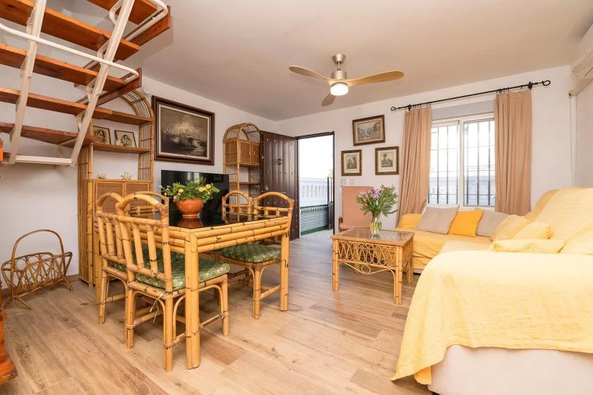 A bright living and dining area with bamboo seating and a bed beside the window.