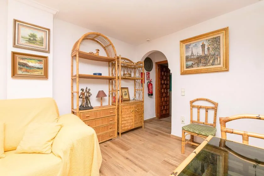 A bright living room with seating, a wooden display cabinet, and framed artwork.
