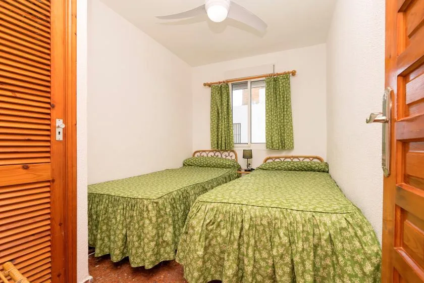 A bedroom with two beds covered in green patterned bedspreads.