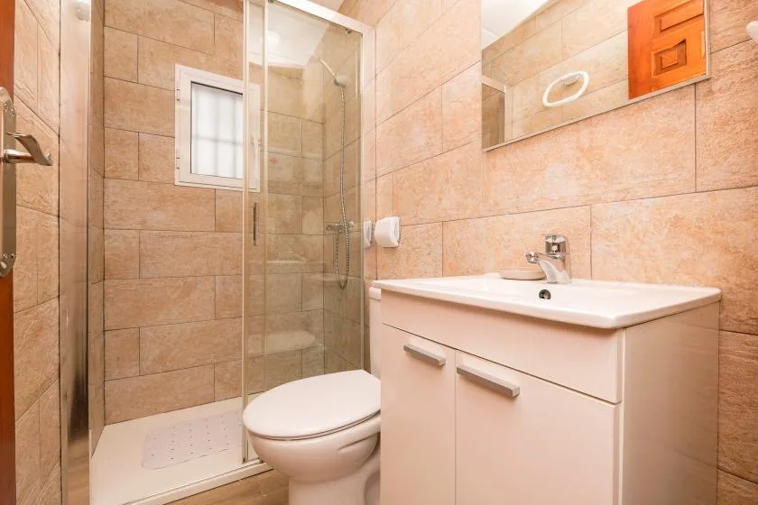 A tiled bathroom with a glass shower, toilet, and sink vanity.