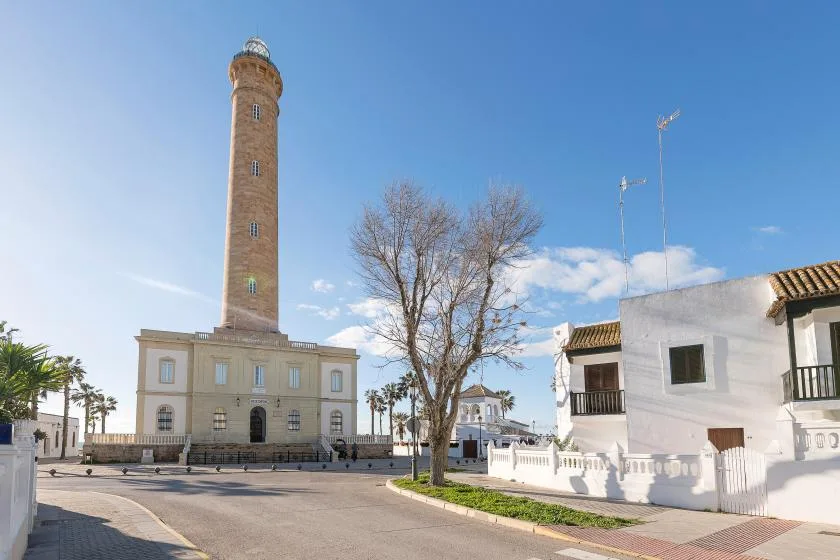 A tall lighthouse rises above low buildings along a sunny street.