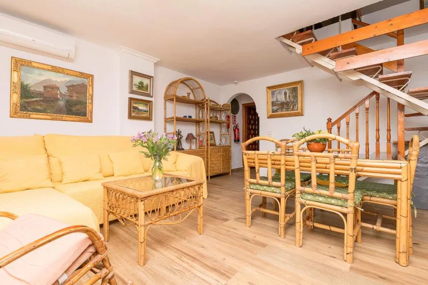 A bright living and dining area with wicker seating and a staircase.