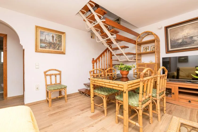 A dining area with a bamboo table and chairs sits beneath an open staircase.