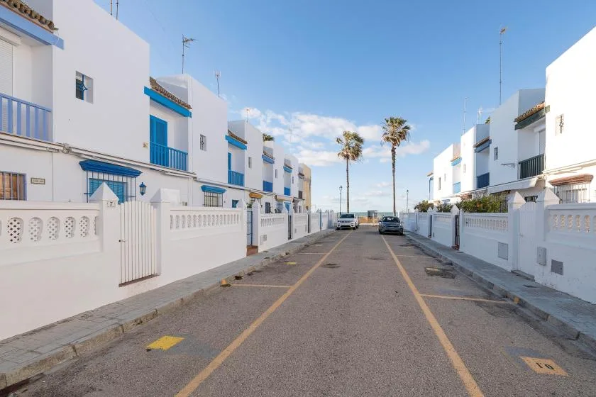 A paved residential street runs between white buildings beneath a clear blue sky.