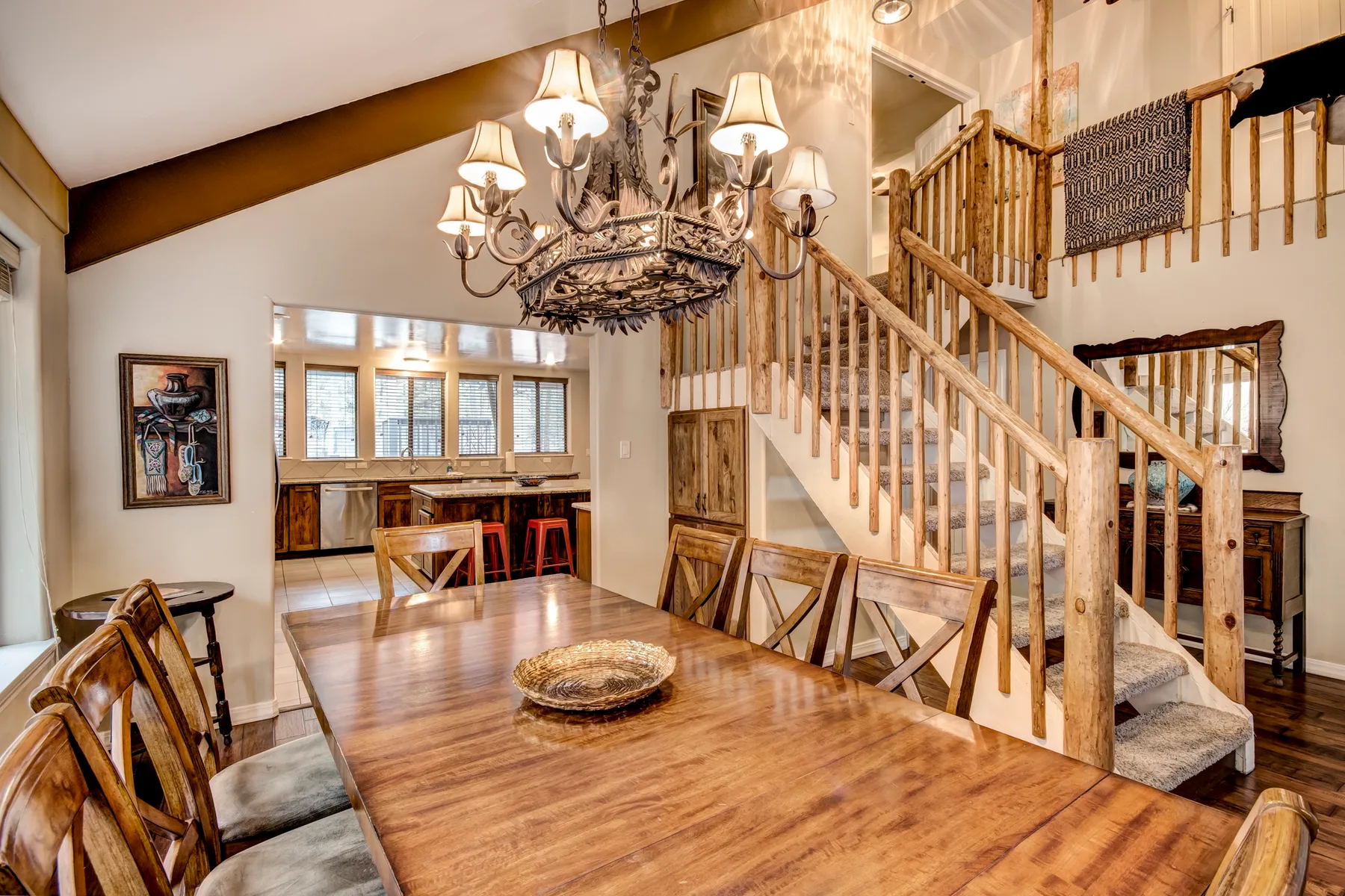 A dining area with a large wooden table beneath a chandelier and a staircase.