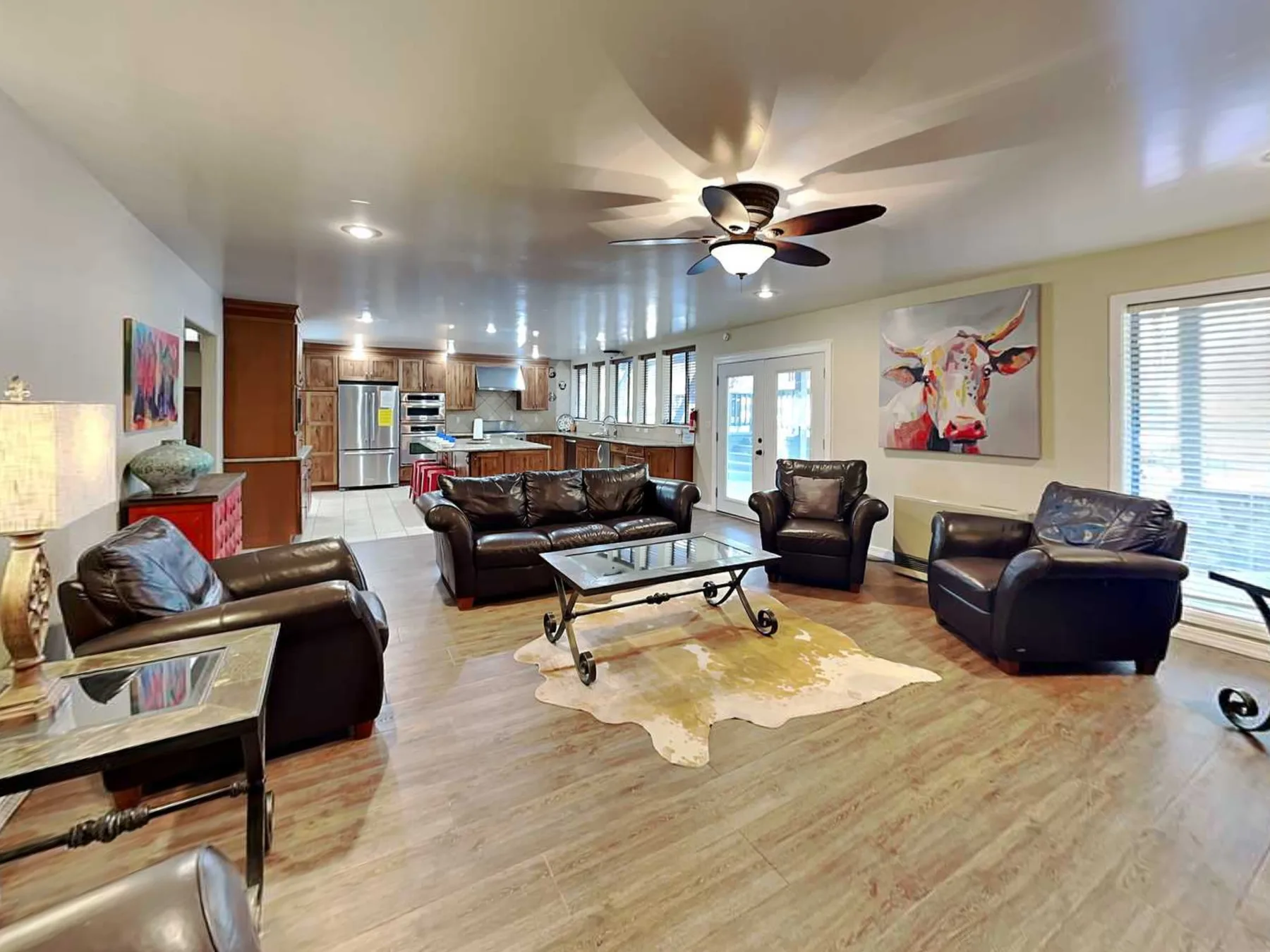 A living room with dark seating, a glass coffee table, and an open kitchen.