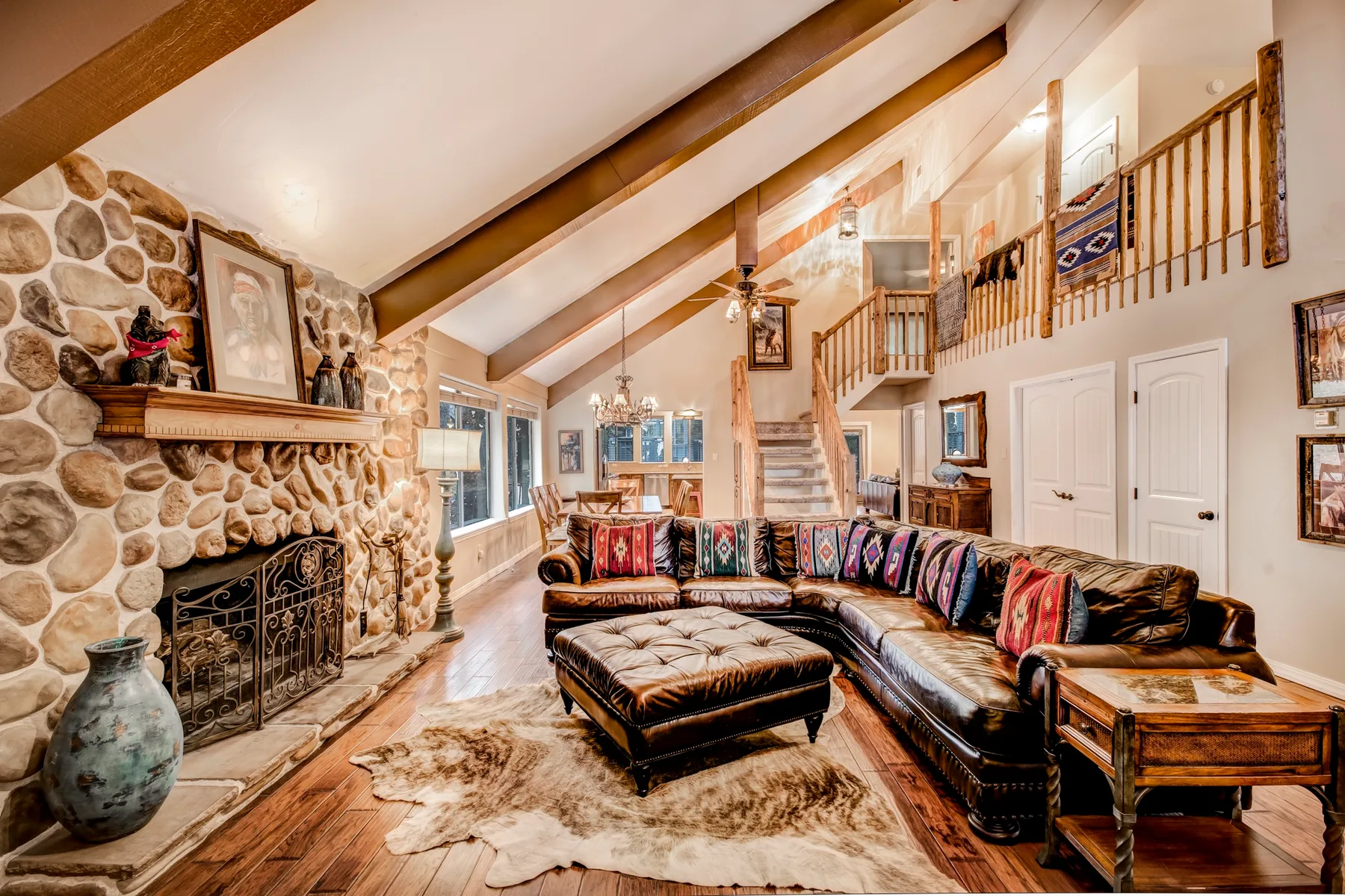 A living room with a stone fireplace, sectional seating, and a loft railing.