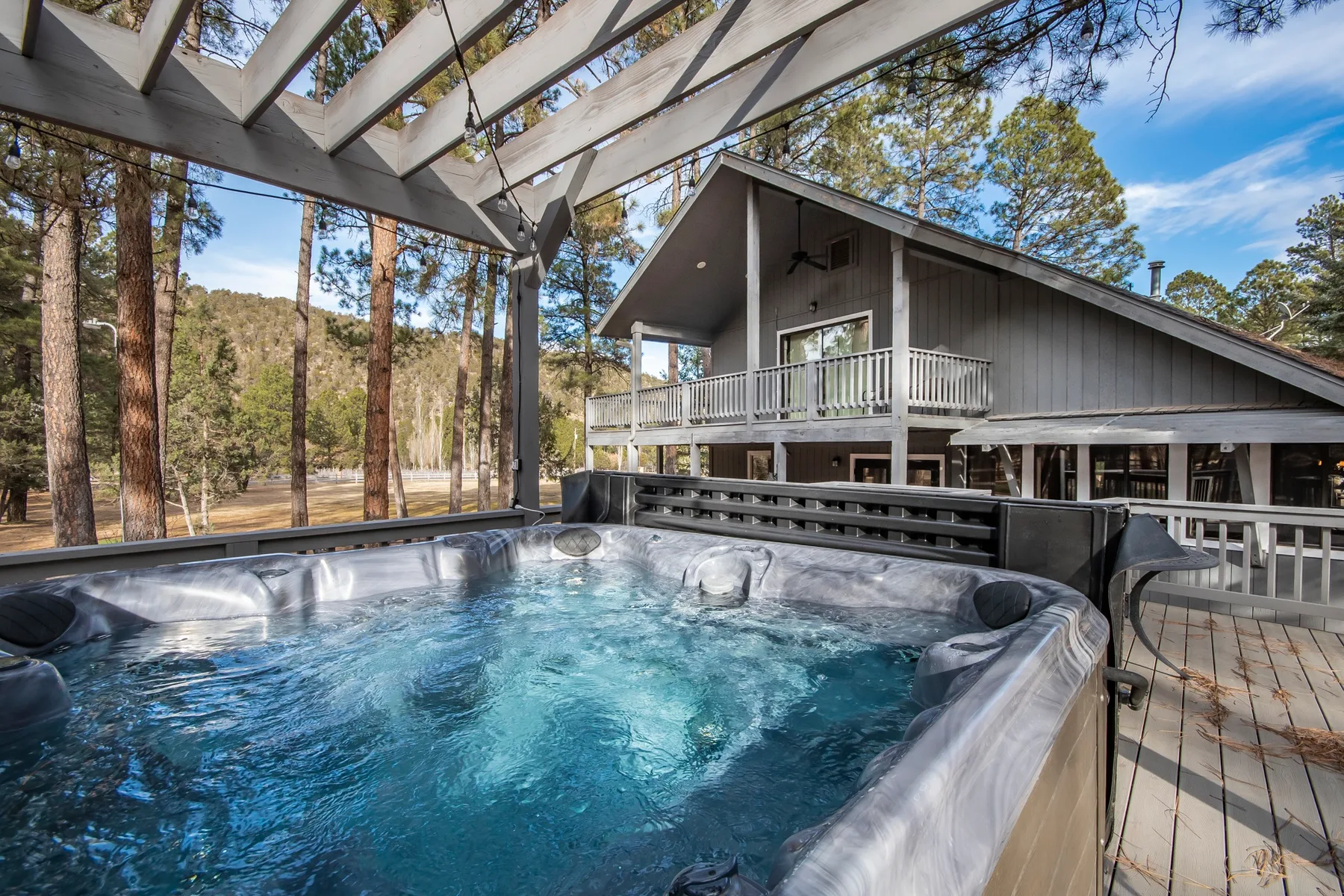 An outdoor hot tub sits on a deck beside a dark wood house.