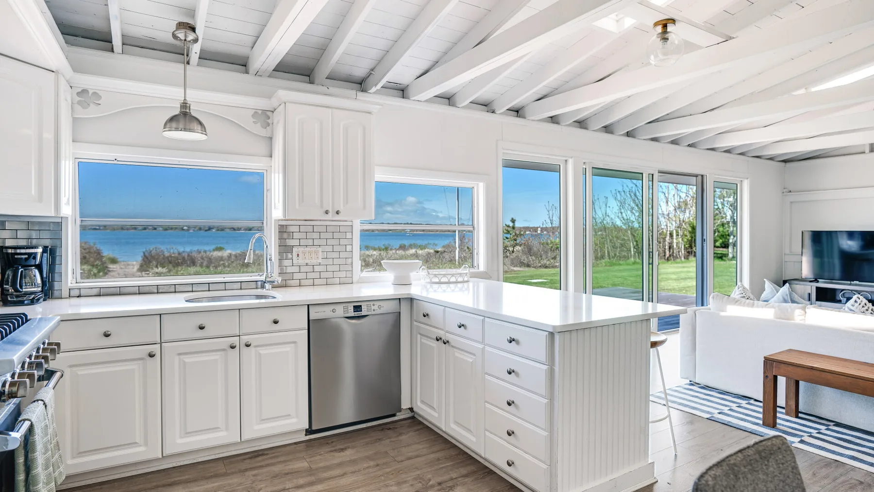 Una cocina blanca y luminosa se abre a un comedor, con grandes ventanas frente al agua.