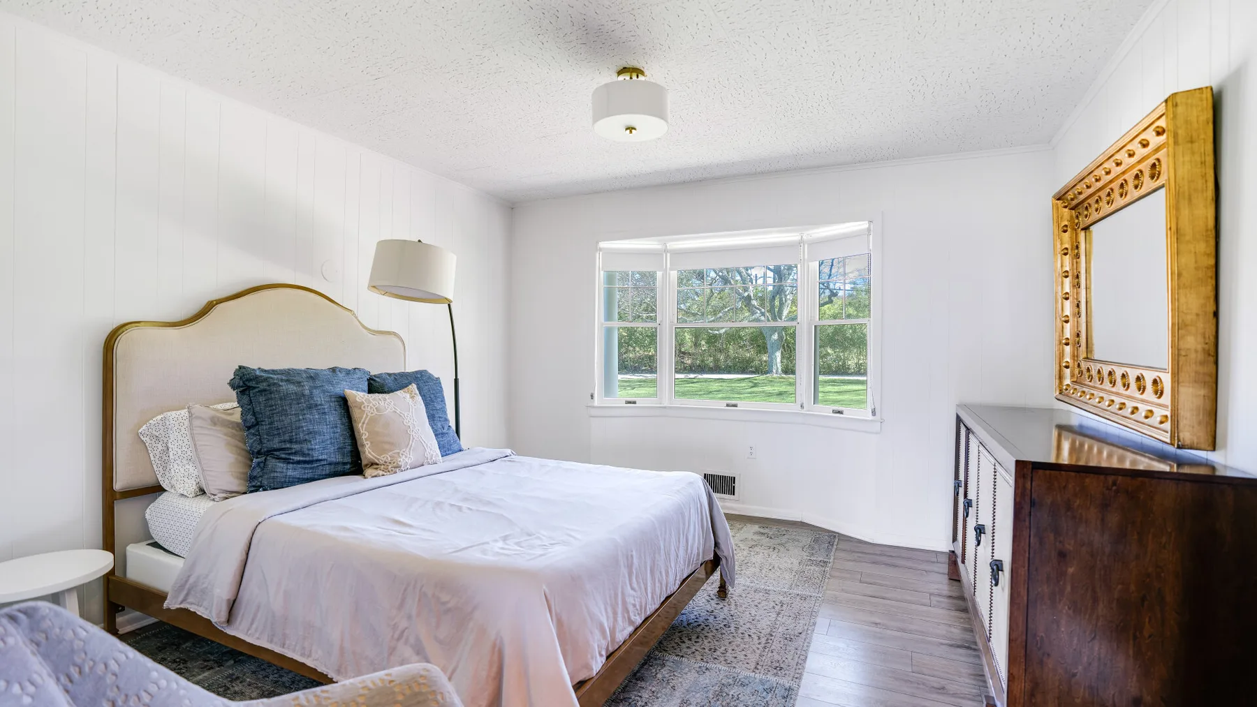Un dormitorio luminoso con una cama bajo una ventana amplia.
