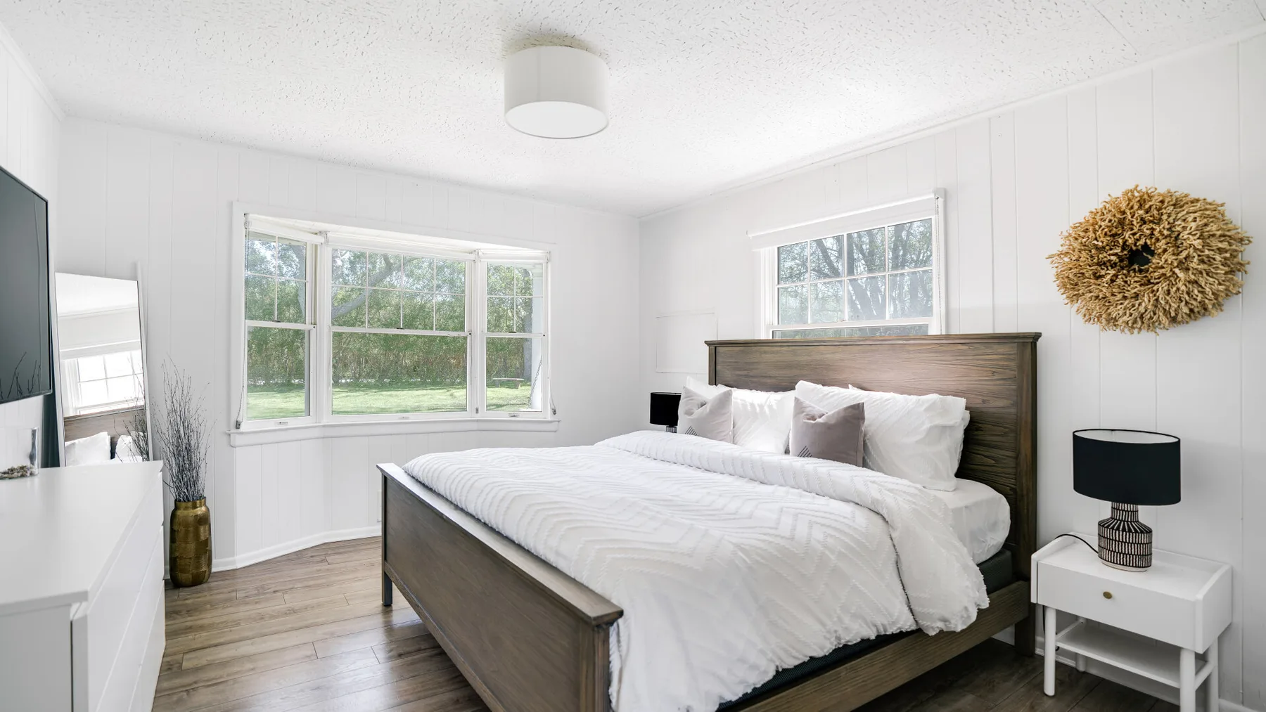 Un dormitorio luminoso con una cama, ropa de cama blanca y ventanas con vistas a la vegetación.