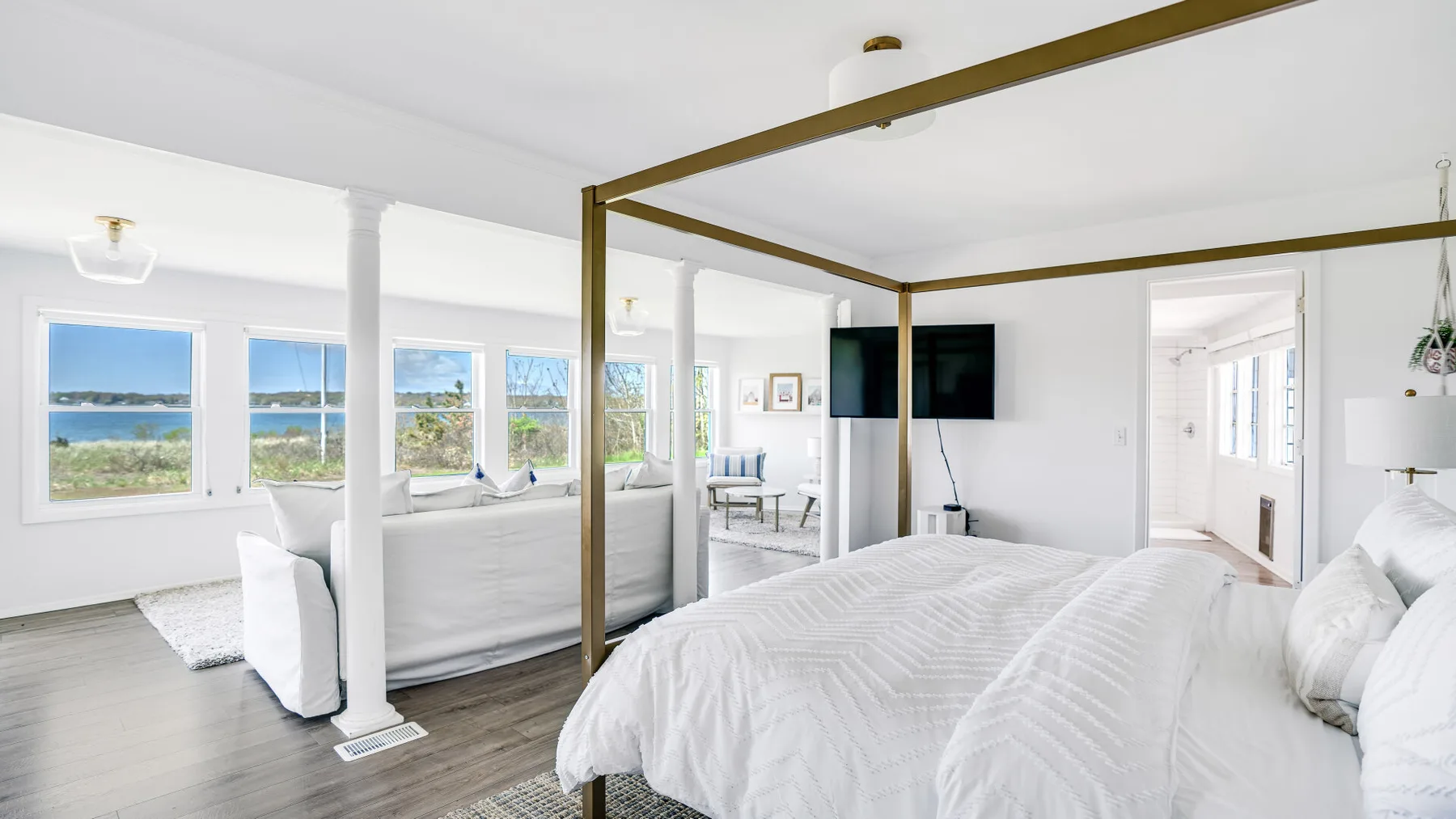 Un dormitorio luminoso con ropa de cama blanca y ventanas con vistas al agua.