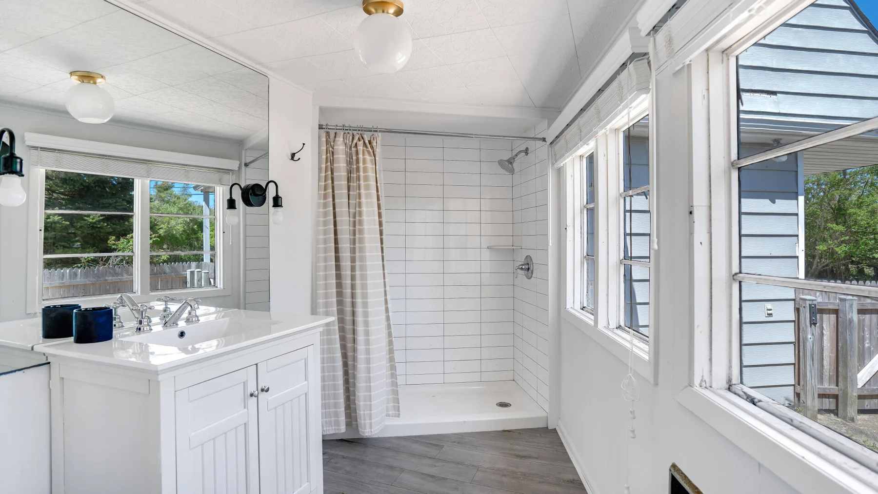 Un baño luminoso con una ducha alicatada y un lavabo blanco junto a grandes ventanas.