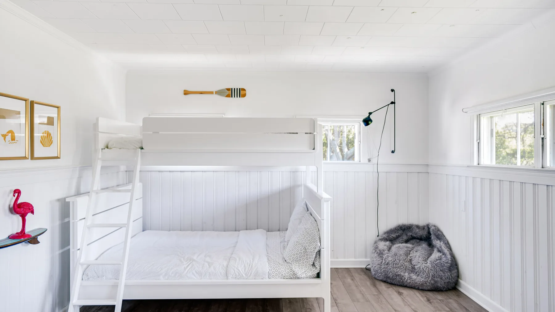 Un dormitorio luminoso con una litera blanca y un cojín gris en el suelo.