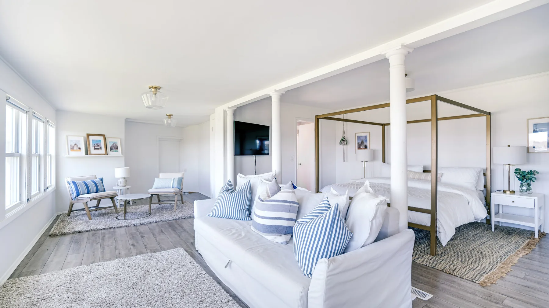 Un dormitorio luminoso con una cama blanca y una zona de estar junto a las ventanas.