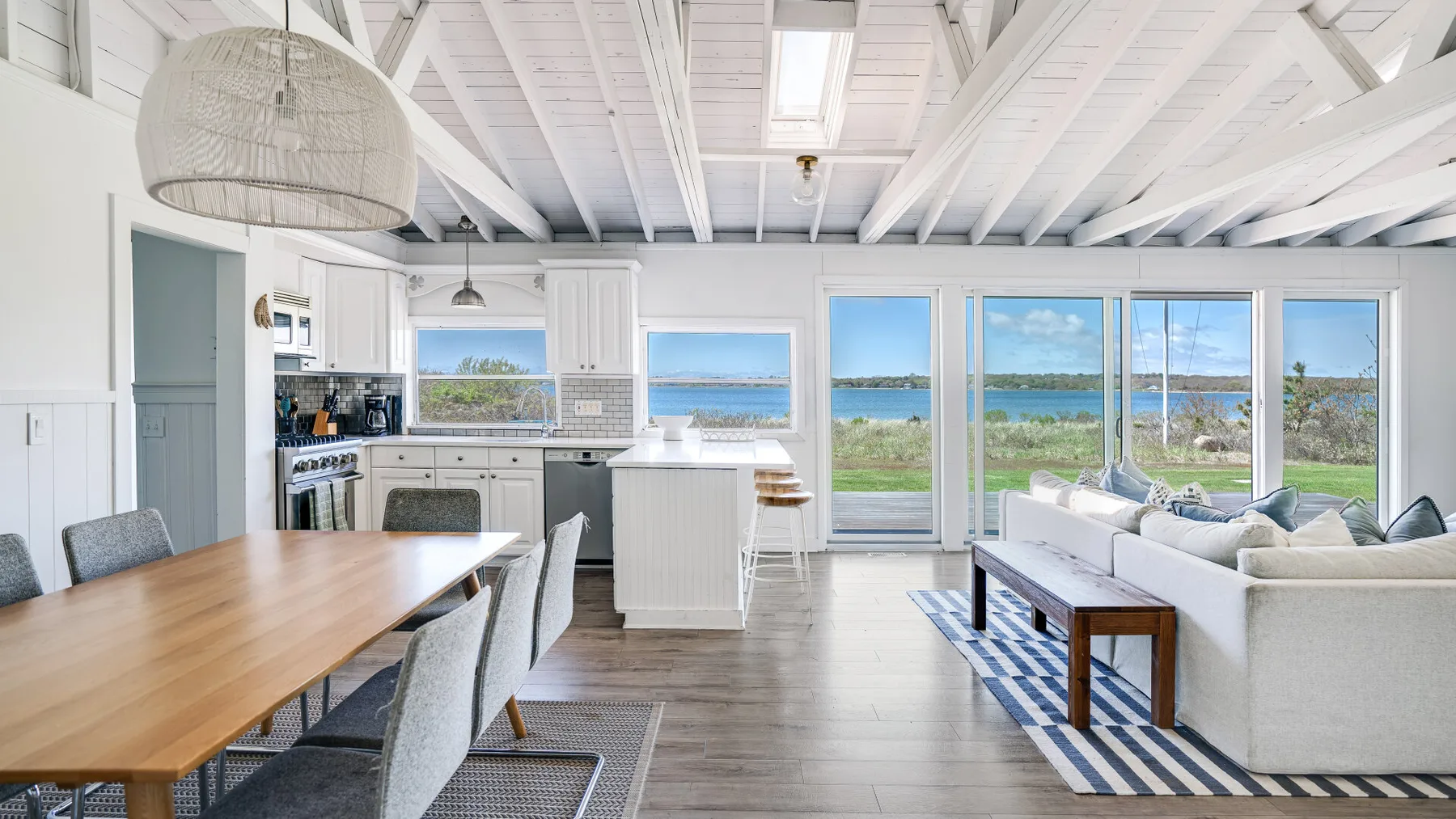 Una sala de estar y cocina de concepto abierto, luminosa y con grandes ventanas frente al agua.