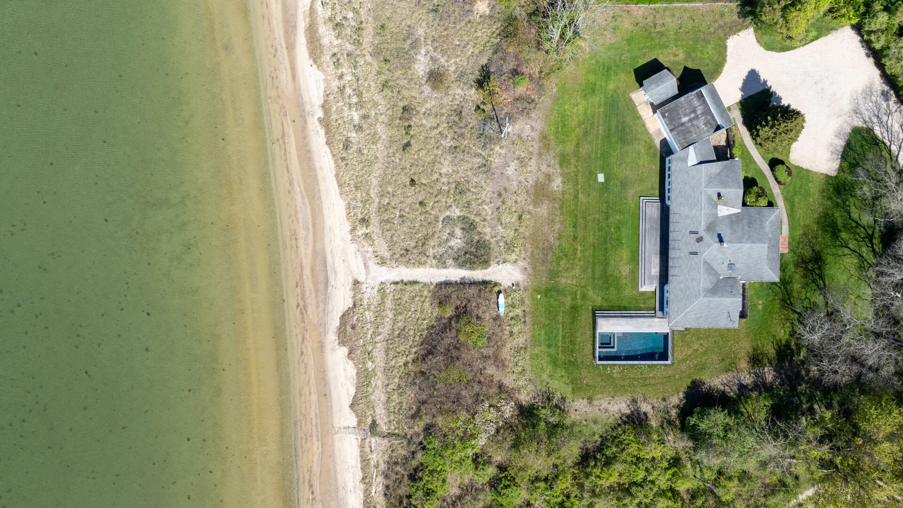Vista aérea de una casa junto a una playa, con una piscina y árboles alrededor.