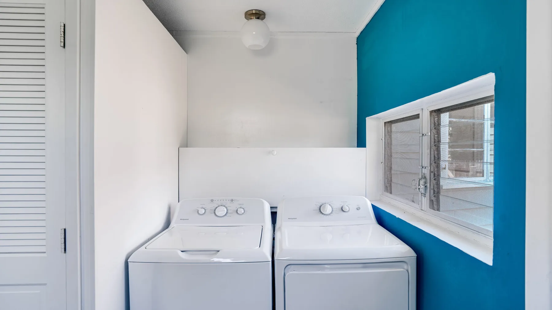 Un cuarto de lavandería con lavadora y secadora debajo de una ventana.