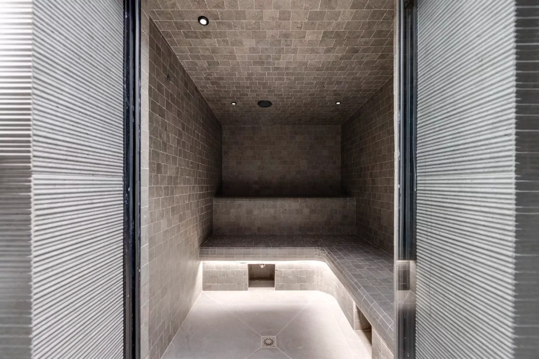 A tiled steam room has a built-in bench and softly lit floor.