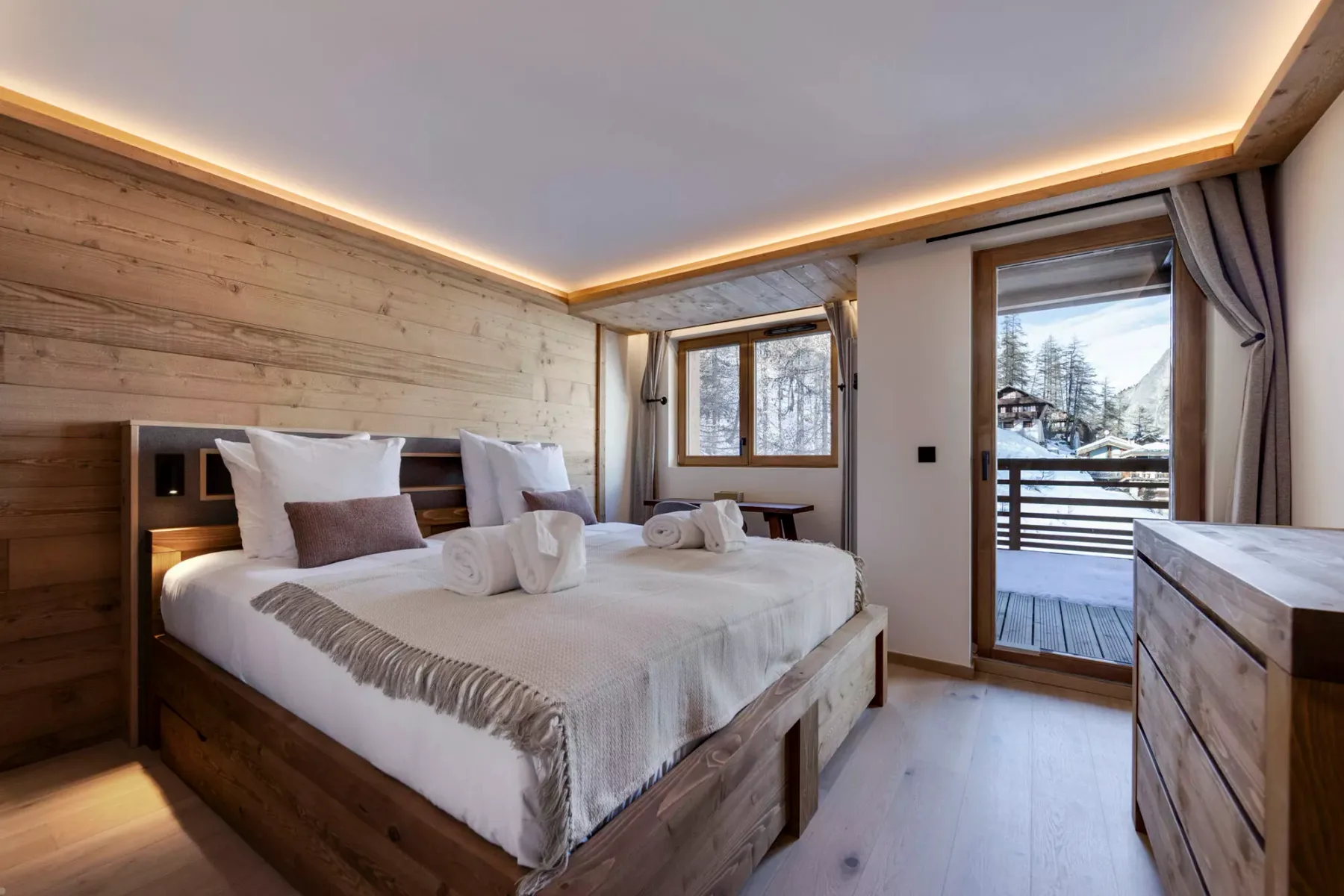 A bedroom with a large bed, wood-paneled walls, and a balcony view.