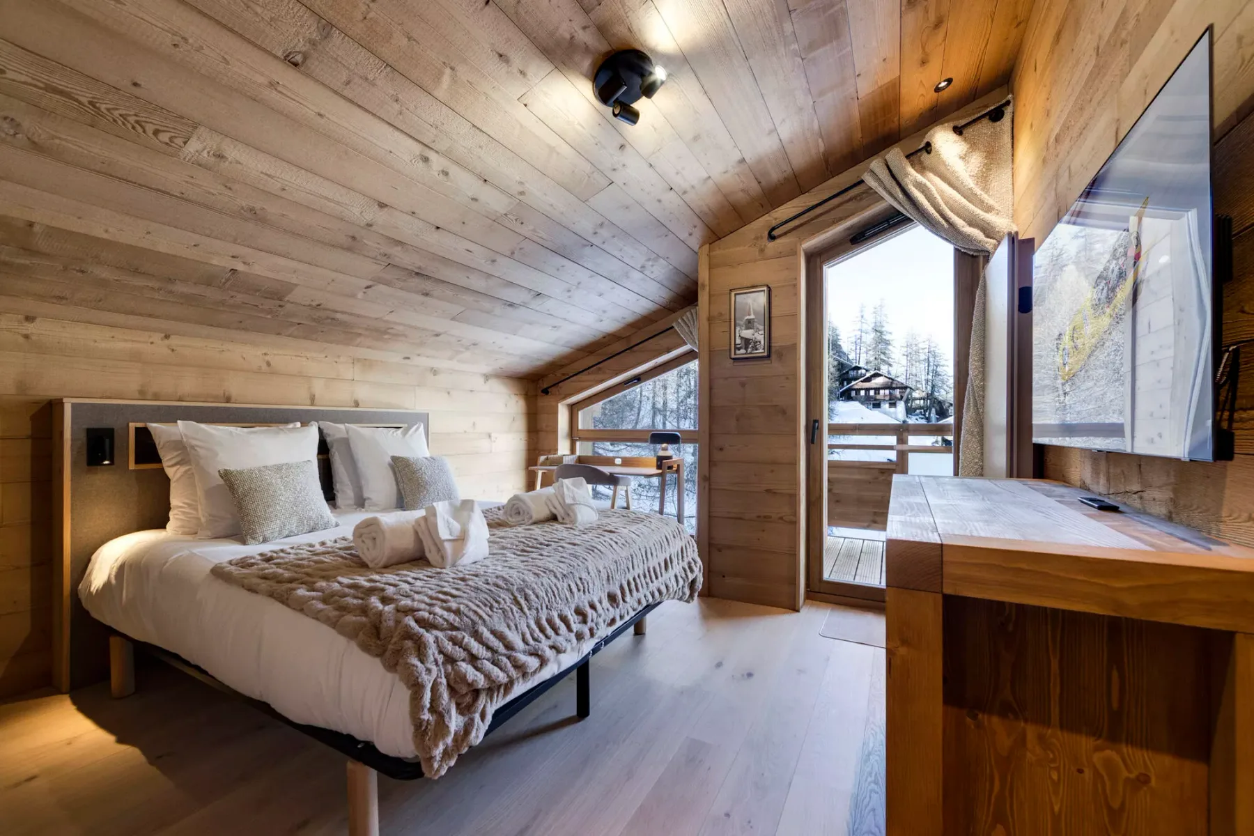 A wood-paneled bedroom with a bed beside a glass door overlooking snowy trees.